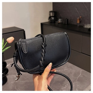Détail d'un sac selle en cuir grainé noir avec bandoulière tressée et breloque poisson