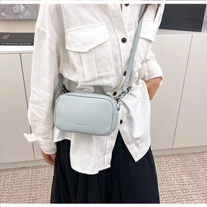 Dettaglio di una borsa a tracolla azzurra in pelle martellata indossata da una modella