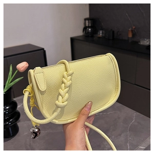Détail du sac selle en cuir litchi jaune avec sangle tressée et breloque coeur argentée