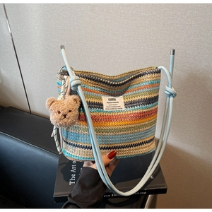 Detail of colorful rainbow woven bucket bag with blue shoulder strap and plush bear charm