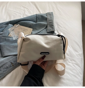 Détail du sac bandoulière en toile beige avec large sangle, logo et fermeture éclair