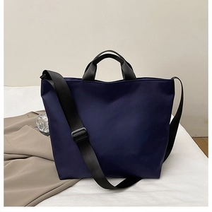 Detail of dark blue nylon tote bag showing adjustable black strap and woven handles