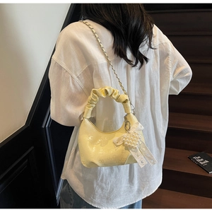 Detail of light yellow ruched crescent bag with embossed texture and pearl heart charm