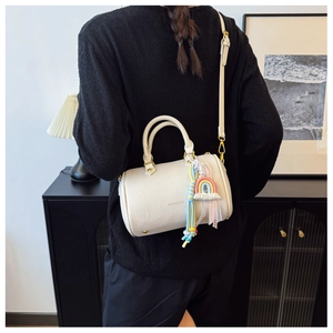 Detailed side view of beige litchi leather barrel bag with rainbow charms and gold hardware