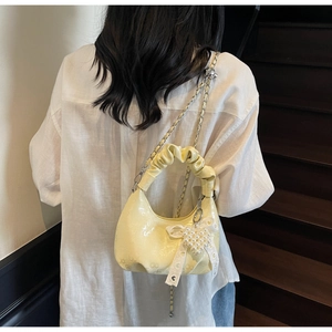 Detail of pale yellow pleated handbag with pearl heart charm and embossed texture