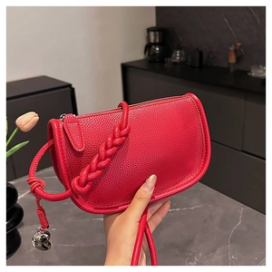 Détail du sac selle en cuir grainé rouge avec poignée tressée et breloque coeur