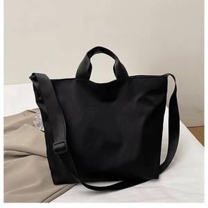 Detail view of large black nylon tote bag with adjustable shoulder strap on white desk