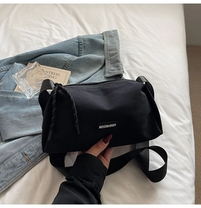 Vue à plat d'un sac bandoulière en toile noire sur lin blanc avec veste en jean