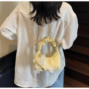 Detail of a yellow pleated handbag with a pearl heart charm and metal chain strap