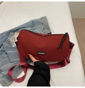 Detail of burgundy crescent shoulder bag with MOONLERSA patch and nylon strap