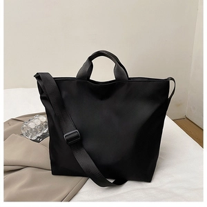 Detail of black nylon tote bag showing wide adjustable shoulder strap and sturdy handles