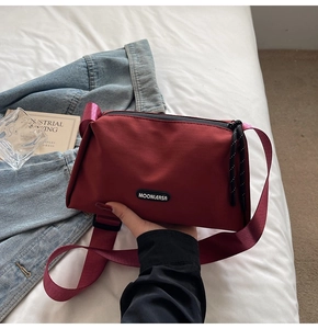 Vue détaillée du sac bandoulière en toile rouge foncé avec large sangle sur le lit