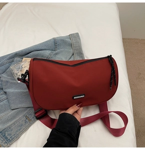 Detail of burgundy crescent moon bag with MOONLEASA logo and wide nylon strap on bed