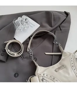 Détail du sac croissant crème avec des clous argentés et une garniture ondulée