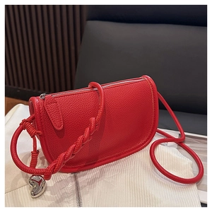Détail du sac selle rouge texture litchi avec bandoulière tressée et breloque cœur