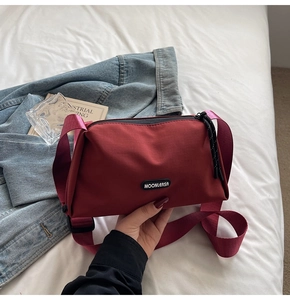 Détail du sac bandoulière en nylon rouge avec sangle large et logo sur un drap blanc