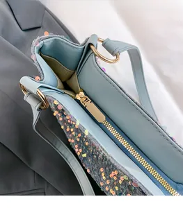Close-up of light blue sequin tote bag showing gold zipper detail and inner leather lining