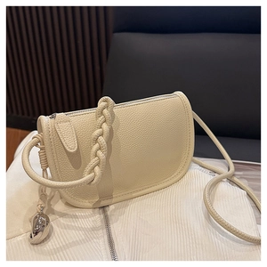 Détail d'un sac selle en cuir grainé beige avec sangle tissée et pendentif argenté