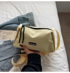 Détail du sac bandoulière en nylon jaune clair avec large sangle et logo de marque noir