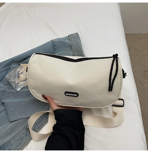 Detail of cream crossbody pillow bag with black zipper and wide fabric shoulder strap