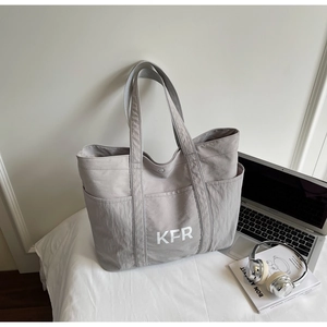 Close-up of a grey canvas tote bag with KFR print and pockets on a white desktop