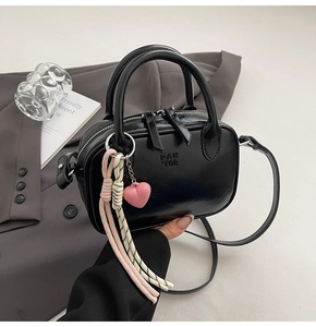 Détail du sac Boston en cuir noir avec logo embossé et accessoire charm cœur rose
