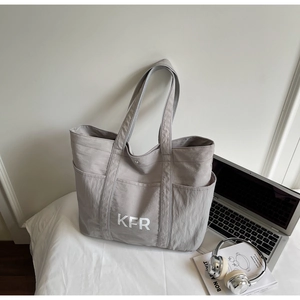Close-up of gray KFR tote bag with side pockets next to a laptop and magazine