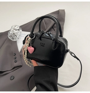 Détail du sac à main noir brillant avec logo embossé sur un blazer gris chic