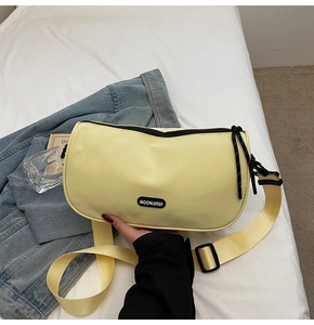 Detail of light yellow nylon pillow bag with black brand logo and adjustable wide strap