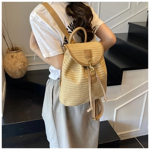 Detailed side view of woven straw backpack with leather straps on a model in sunlight