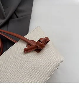 Détail d'un sac cabas en toile crème avec anse en cuir marron et détail de nœud décoratif