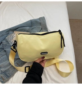 Detailed shot of yellow nylon pillow bag with black logo patch and woven shoulder strap