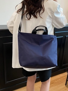 Minimalist navy large tote bag with black handles shown on a model in a white suit