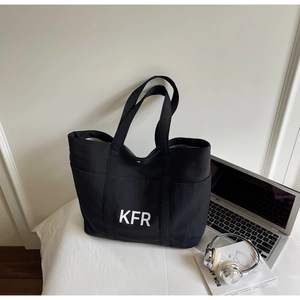Detail view of large black canvas tote bag with KFR print beside a laptop and headphones