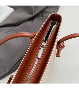 Détail de la fermeture éclair argentée sur un sac cabas en toile beige et cuir brun
