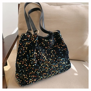 Close-up of sparkling black sequin tote bag with gold ring hardware on a beige chair