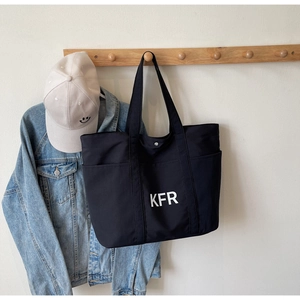 Detail view of black canvas tote bag with white KFR lettering on wood hook