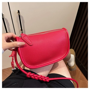 Détail du sac selle en cuir rouge avec bandoulière tressée et breloque en perle argent