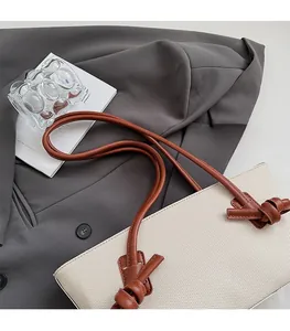 Gros plan sur la bandoulière en cuir nouée contrastée d'un sac cabas tissé crème