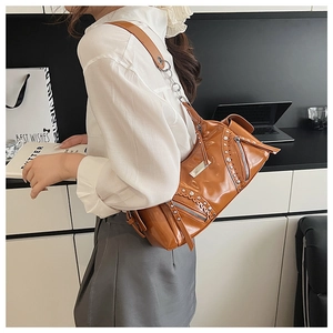 Détail du sac croissant en cuir marron avec rivets argentés et bandoulière en chaîne