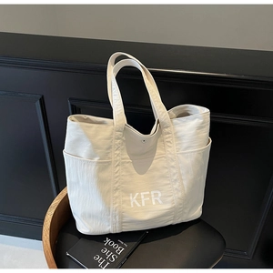 Detail of off-white canvas tote bag with KFR print and magnetic buckle on a chair