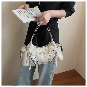 Détail du sac crème avec rivets, finition brillante, fermetures éclair et chaîne métal