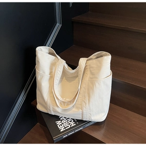 Detail view of large cream canvas tote bag with side pockets on a wooden staircase