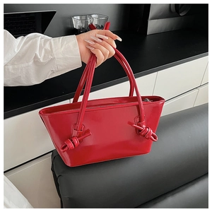 Vue détaillée du sac cabas en cuir verni rouge avec poignées à double nœud et fini brillant