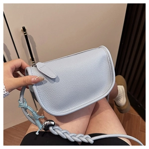 Détail du sac selle bleu clair avec texture en cuir grainé et bandoulière tressée