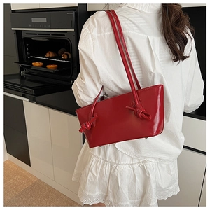 Détail du sac à bandoulière en cuir verni rouge brillant avec nœud décoratif sur la sangle
