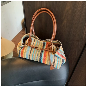 Detail of colorful striped straw shoulder bag with brown leather handles on leather chair