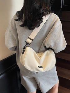 Chic beige crescent crossbody bag with wide nylon strap shown on model outdoors