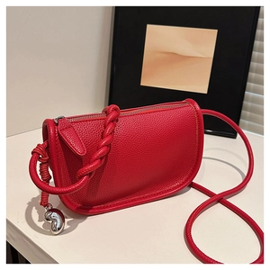 Détail du sac selle en cuir grainé rouge avec bandoulière tressée et pendentif argent