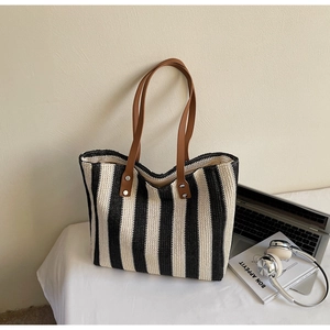 Detail of striped straw tote bag with brown leather handles and silver rivets on desk